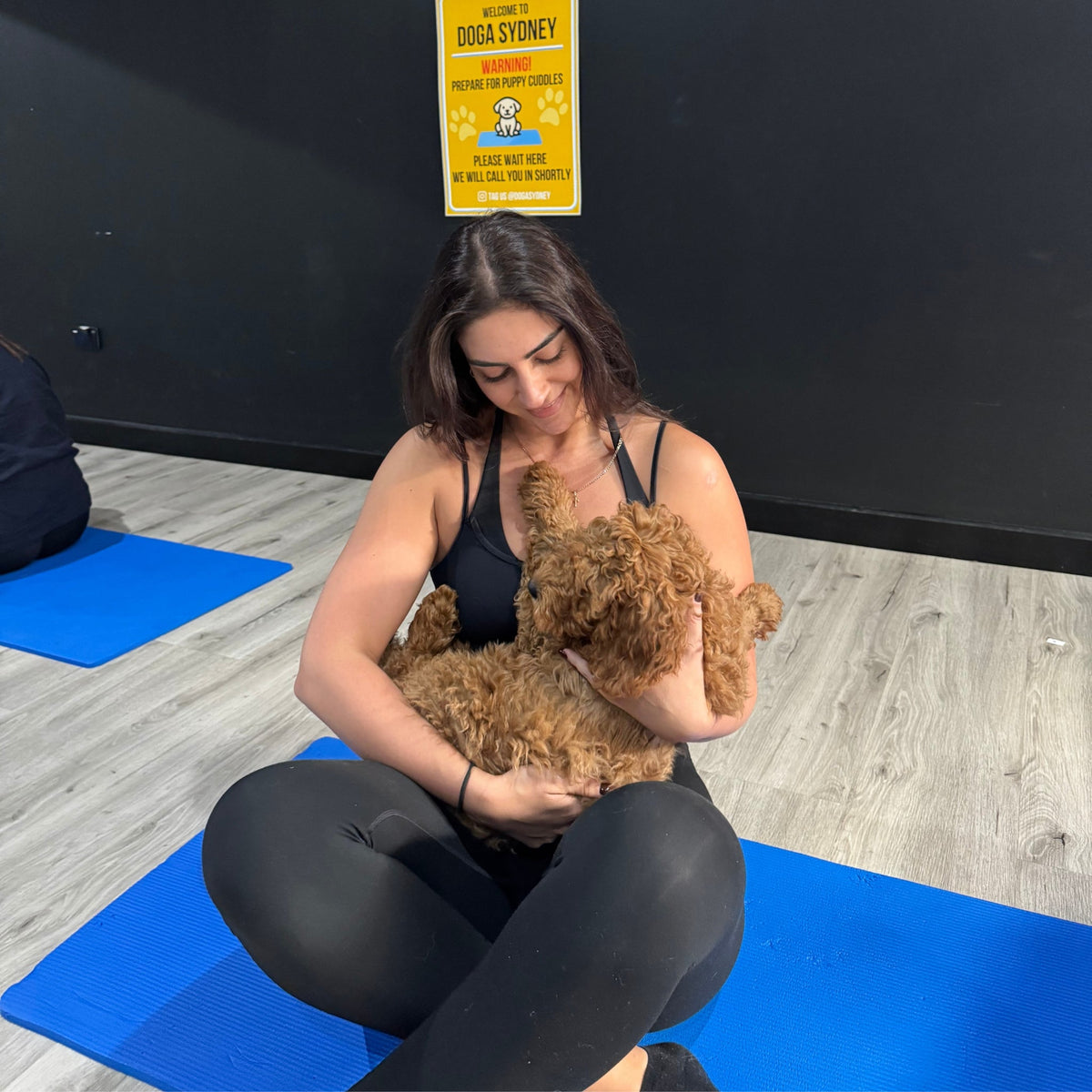 A woman on her yoga mat cuddling a red cavoodle puppy