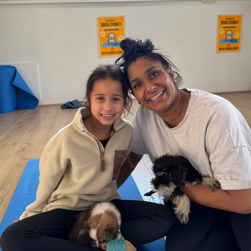 A girl and a woman on yoga mats with two small fluffy puppies
