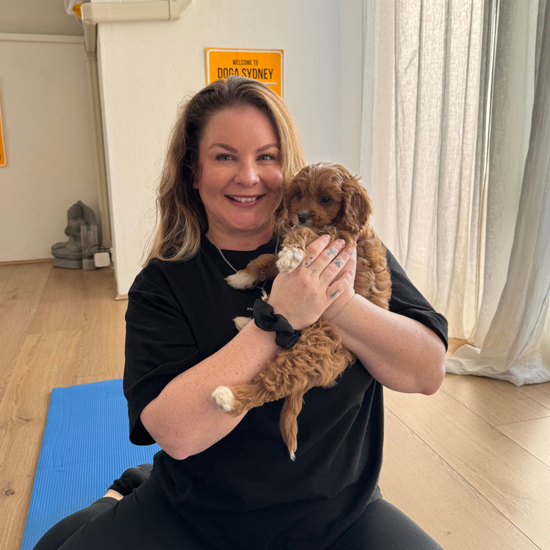 A woman holding a red cavoodle puppy close to her face