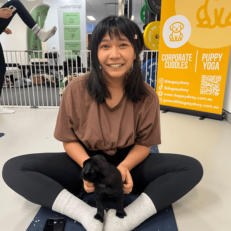 A woman sitting cross-legged with a black puppy in her lap