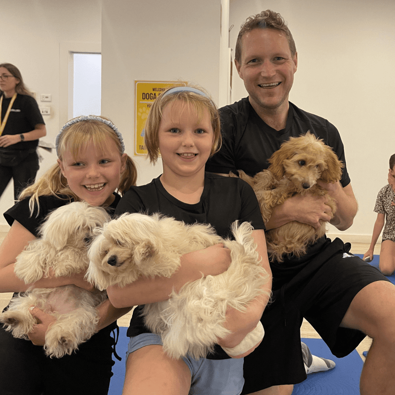 Two girls and a man holding three fluffy puppies at puppy yoga
