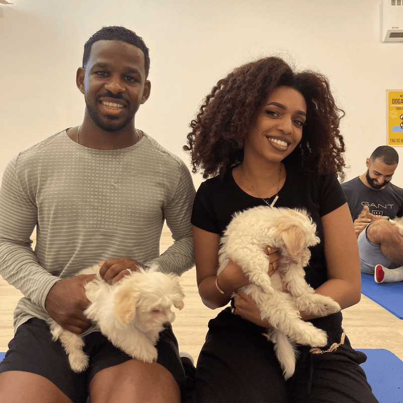 A couple on yoga mats, each holding a small cream puppy