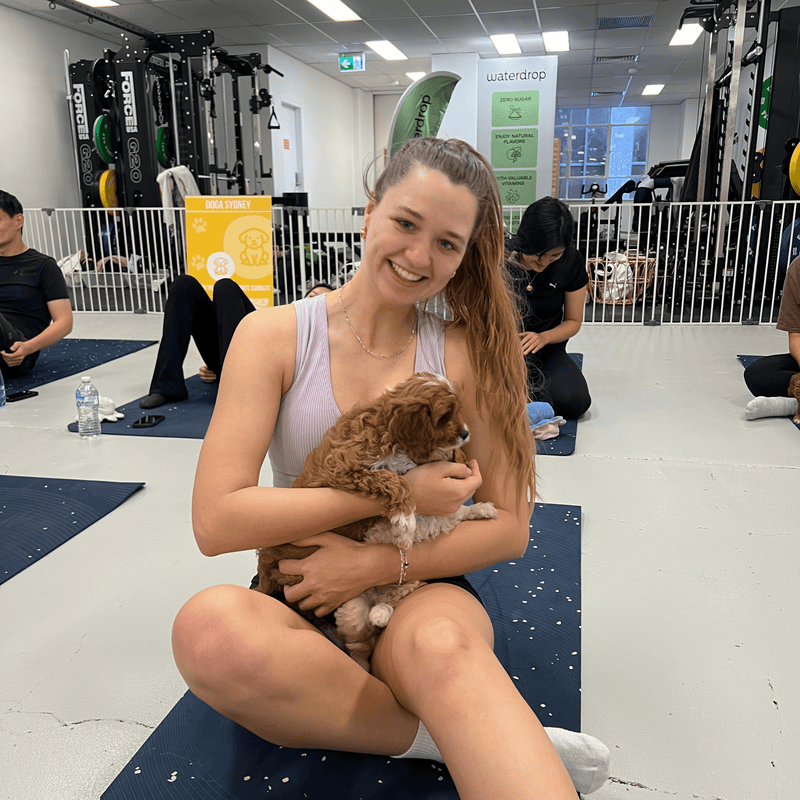 A woman on her yoga mat hugging a brown and white puppy