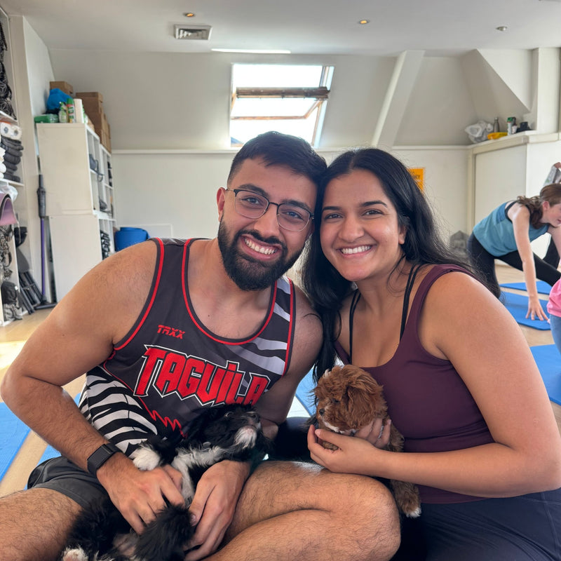 A couple on yoga mats with a black and white puppy and a brown puppy