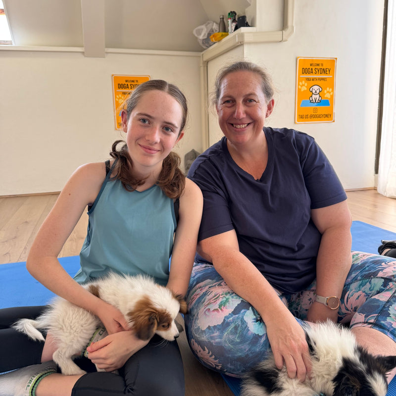 A girl and a woman on yoga mats with two white and tan puppies