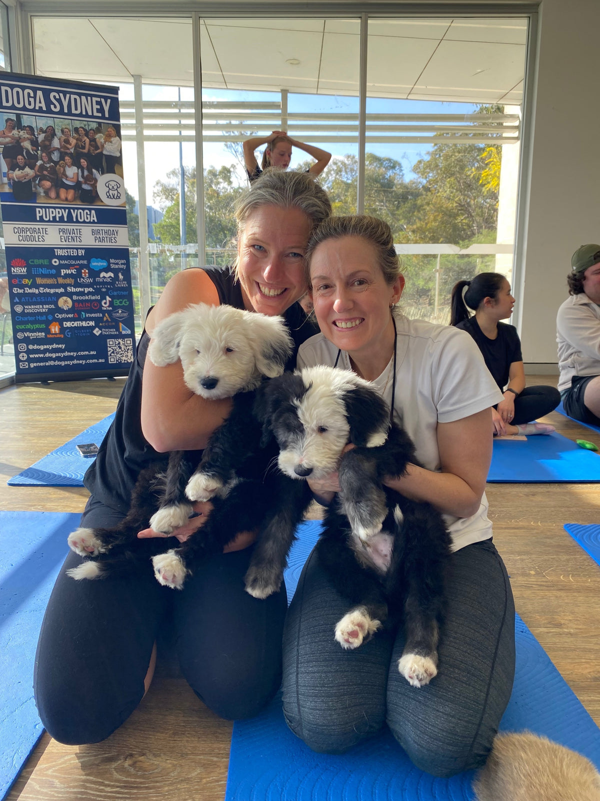 Two friends holding fluffy puppies on yoga mats at a Doga Sydney class