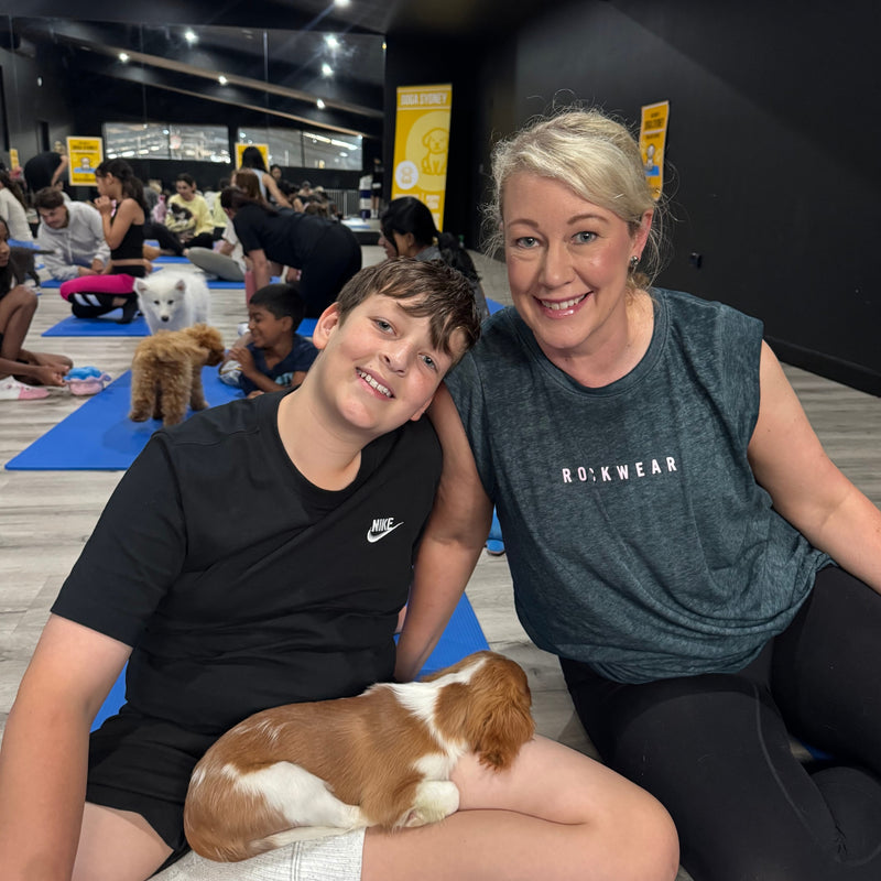 A boy and a woman on yoga mats with a cavalier puppy resting in his lap